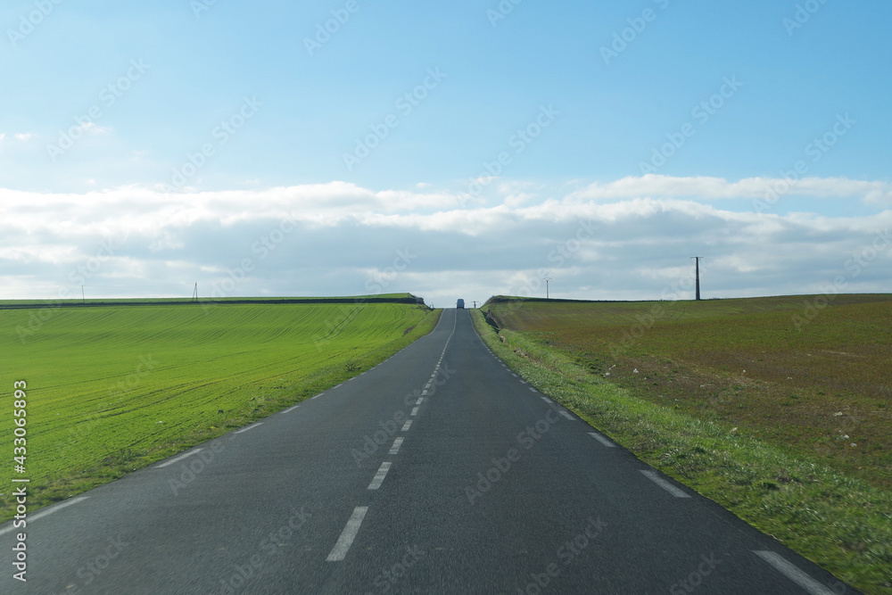 Asphalt road through the green field and clouds on blue sky in summer day.