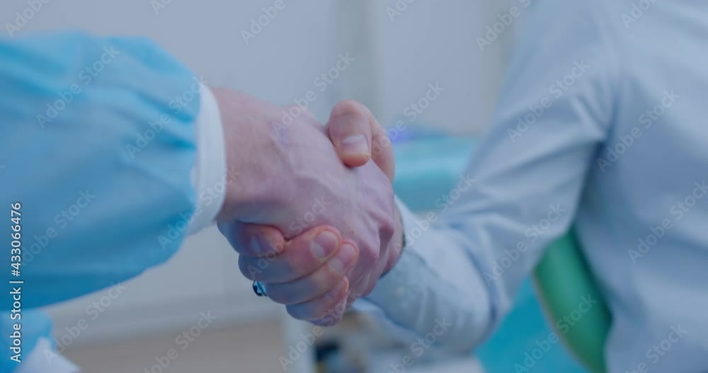 Close-up a shaking hands of a male patient and male dentist that are sitting in the dental room. Close-up a shaking hands of a male patient and male dentist that are sitting in the dental room.