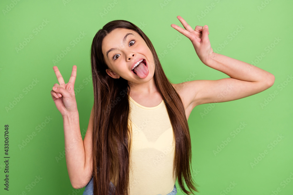 Photo of cheerful excited girl tongue out fingers show v-sign have good mood isolate don green color background Photo of cheerful excited girl tongue out fingers show v-sign have good mood isolate don green color background