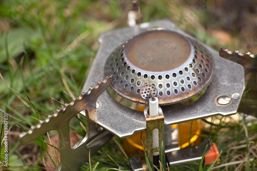 Close-up of a portable camping gas stove. The burner is on the grass.