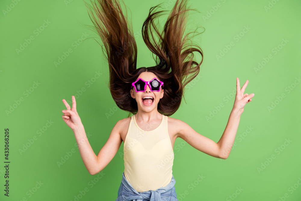 Photo of happy excited crazy cheerful smiling girl with flying hair funny sunglass showing v-sign isolated on green color background