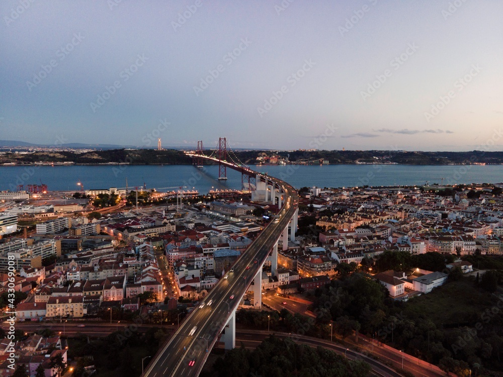 Aerial view of April 25th bridge with Christ the King statue (Cristo Rei) in background at sunset, view of Lisbon skyline at night, Alcântara, Lisbon, Portugal.