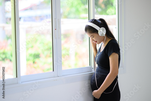 A pregnant woman in a black dress, wearing a white headphones, stood listening to music by the window.A pregnant woman standing by the window listening to nostalgic music Free Download A pregnant woman in a black dress, wearing a white headphones, stood listening to music by the window.A pregnant woman standing by the window listening to nostalgic music - GFXLoad