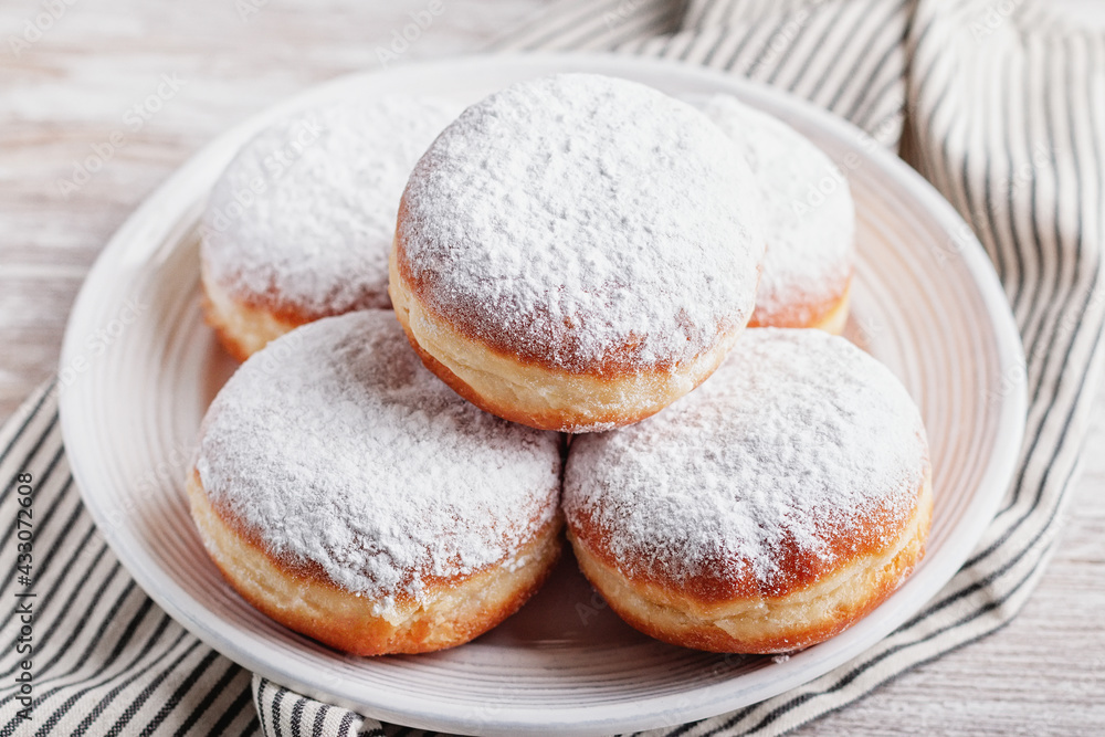 Delicious strawberry jam filled berliner doughnuts on white plate with napkin on wooden table top overhead Delicious strawberry jam filled berliner doughnuts on white plate with napkin on wooden table top overhead