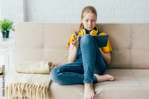 Cuadro en lienzo Red-haired cheerful schoolgirl teenager with a digital tablet at home on the couch studies does homework