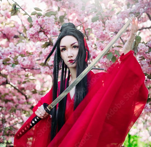 Portrait of young woman in image of geisha with sword in her hand near blooming sakura trees Fototapet