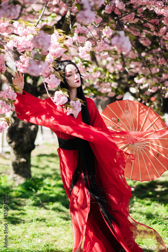 Young woman in image of japanese geisha walks between blooming sakura trees.