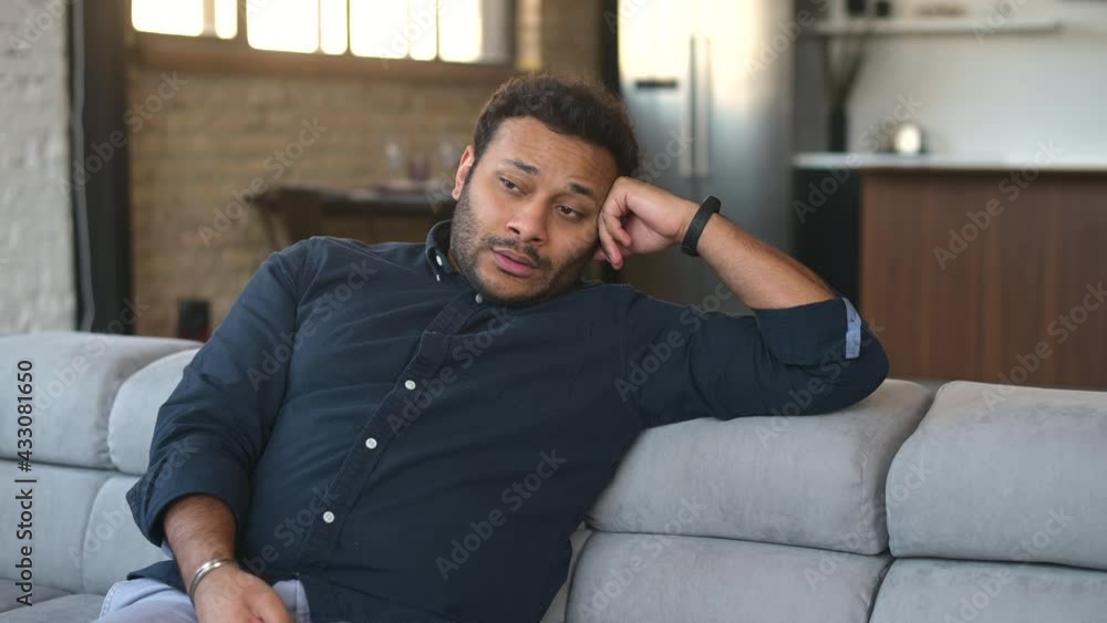 Bored young indian man sitting on the couch watching TV, mixed race man switching channels, feels sadness and loneliness, lazy guy spends weekend with tv shows Bored young indian man sitting on the couch watching TV, mixed race man switching channels, feels sadness and loneliness, lazy guy spends weekend with tv shows
