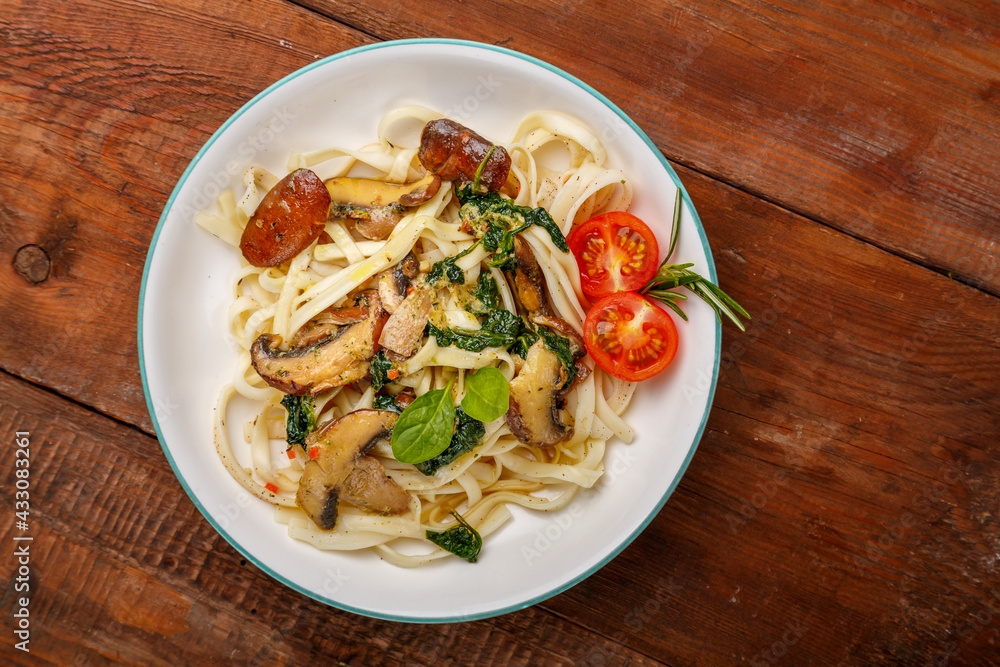 Udon with mushrooms and spinach and cherry tomatoes in a plate on a wooden table. Udon with mushrooms and spinach and cherry tomatoes in a plate on a wooden table.