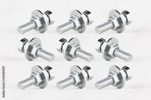 Texture and repetitive pattern of screws, nuts and washers, created by photo composition, on a white background. All the pieces are identical, but look in different directions.