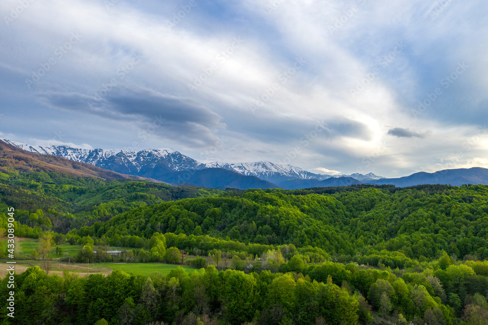 Sunny mountain scenery with vivid green forest on hill and snowy mountains in sunlight in low clouds. Sunny mountain scenery with vivid green forest on hill and snowy mountains in sunlight in low clouds.
