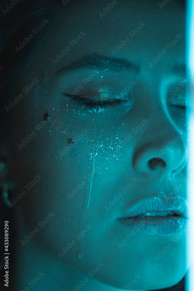 crying woman with sparkles makeup and light cyan color