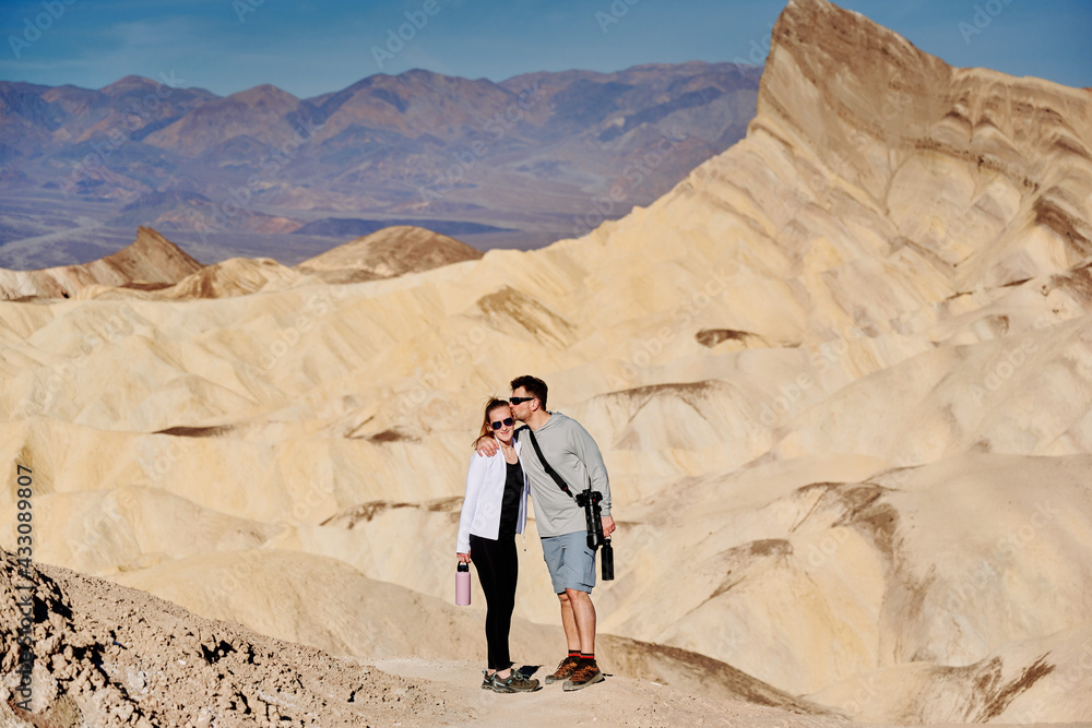 A family hike from Zabriskie Point in Death Valley national park in california. Huge sand dunes, terracotta mountains and hazy horizons are shining against clear blue sky in the midday sun.