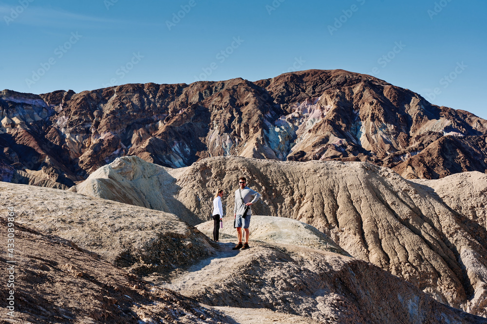 A family hike from Zabriskie Point in Death Valley national park in california. Huge sand dunes, terracotta mountains and hazy horizons are shining against clear blue sky in the midday sun.