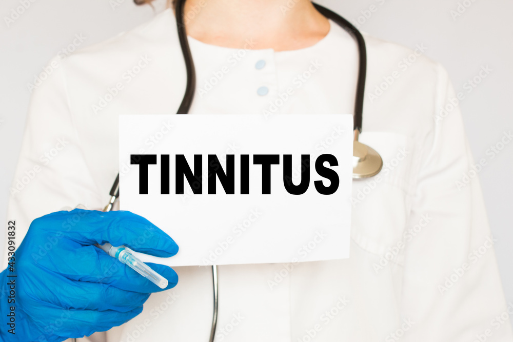 the doctor in gloves holds a card with the text TINNITUS . white background. the medicine the doctor in gloves holds a card with the text TINNITUS . white background. the medicine