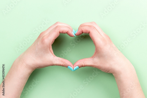 Female hands with mint blue nails making heart symbol on green background