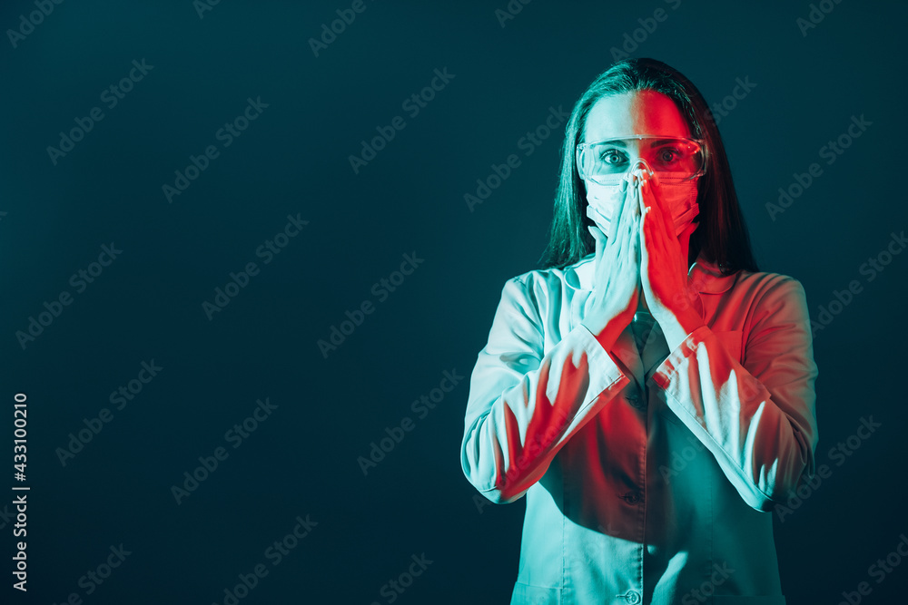 Shocking healthcare. Medical mistake. Pandemic panic. Scared female doctor in face mask goggles with omg reaction in red neon light isolated on teal blue empty space background.