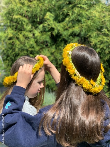 Two girls put dandelion wreaths on their heads.