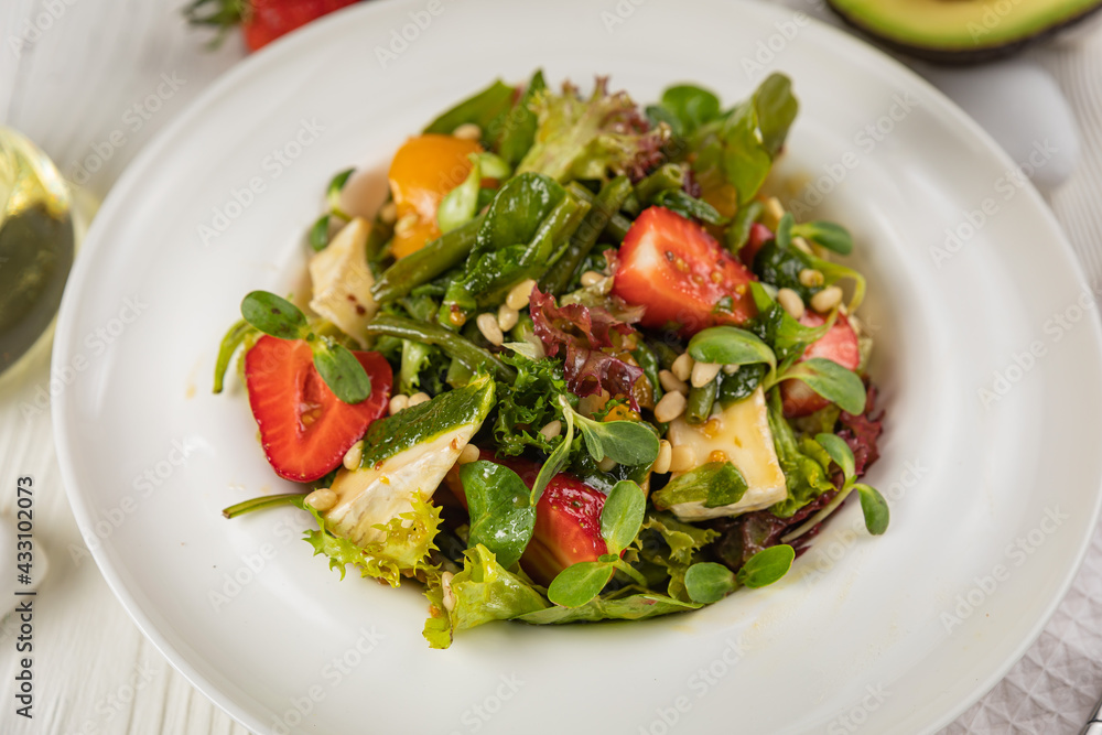 Salad with strawberries, brie cheese, tomatoes and greens. On a white plate and white table.
Salad with strawberries, brie cheese, tomatoes and greens. On a white plate and white table.