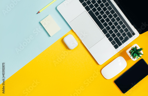 top view of laptop, cactus, mobile phone, computer mouse, pencil on yellow and blue background with free space for text
