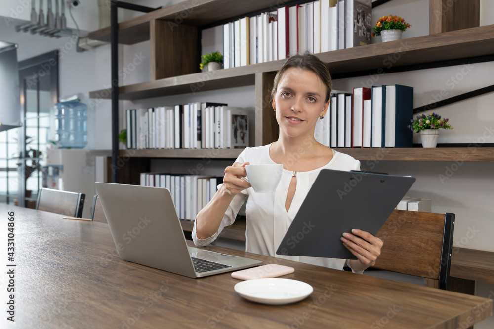 Female drinking coffee at wooden table with notebook computer in a cafe. Business woman with coffee and computer laptop working. Female drinking coffee with smiles while enjoying her leisure time.