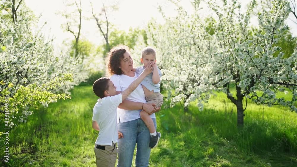 mother with sons walks in flowering garden. youngest child in her arms