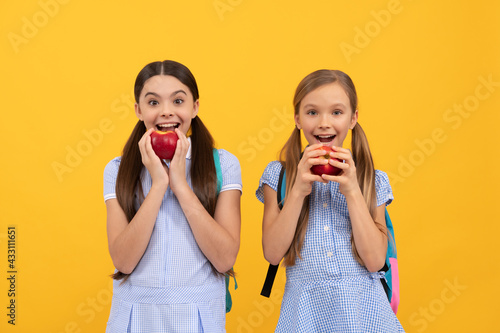 Happy teenage school children eat vitamin organic apples yellow background, school nutrition