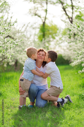 mother with sons kiss and cuddle in flowering garden. mother's day