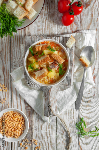 Pea soup with bacon and croutons on a white wooden board in light colors