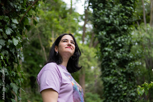 Photo of an attractive woman with black hair in the middle of nature during spring time, walking around and smiling during a sunny day