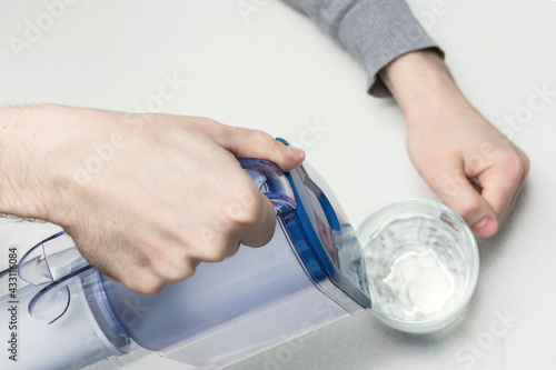 Pouring water from filter jug into glass in the kitchen, top view