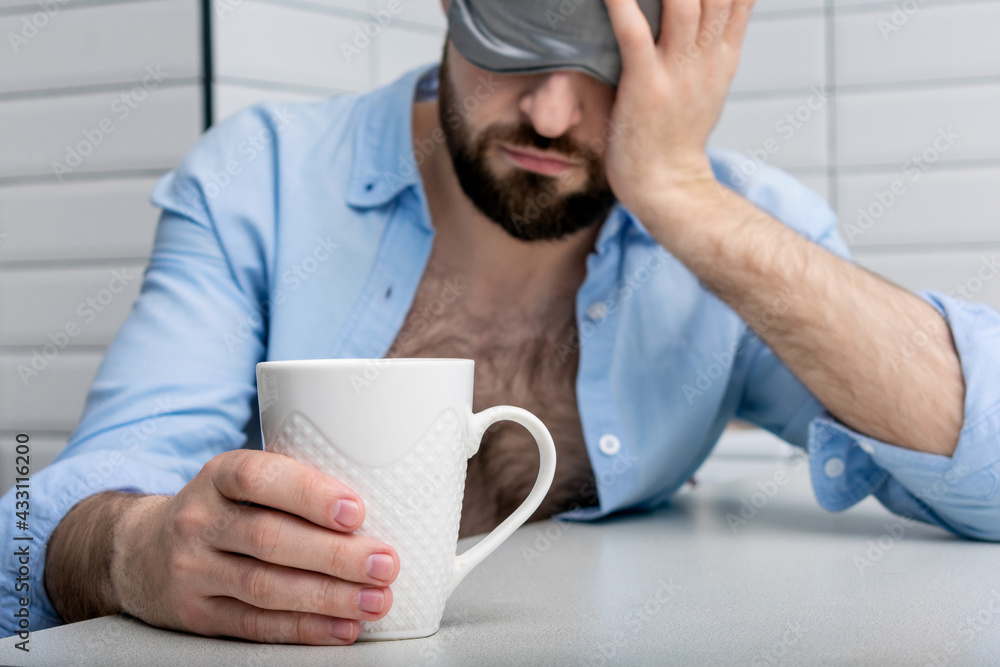 Sleepy man with a cup of coffee in the morning, man in a sleep mask can't wake up, close-up, cropped image Sleepy man with a cup of coffee in the morning, man in a sleep mask can't wake up, close-up, cropped image