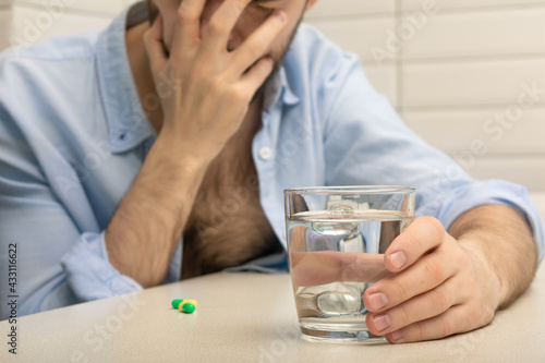 Drunk man has a headache, pain pills and a glass of water, close-up, cropped image