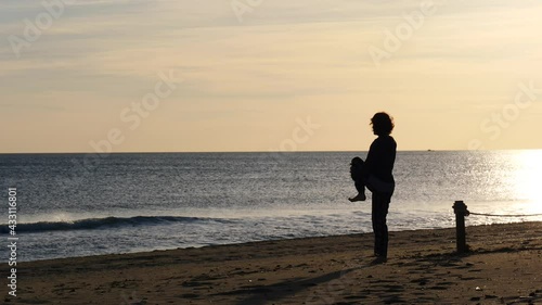 Woman barefoot at morning time on beach. Female stretching, doing sports outdoors. Slow motion. Active living concept. Taking care of health. Reducing stress by exercising. photo