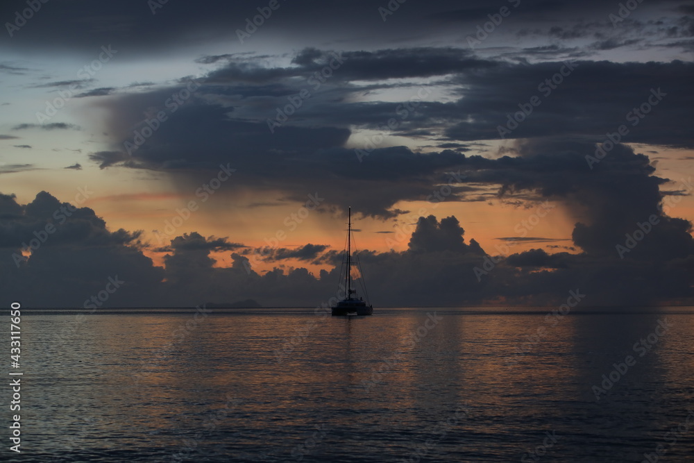 Yacht at sea at sunset with stormy black-orange sky. Background image of ship standing at night in the bay