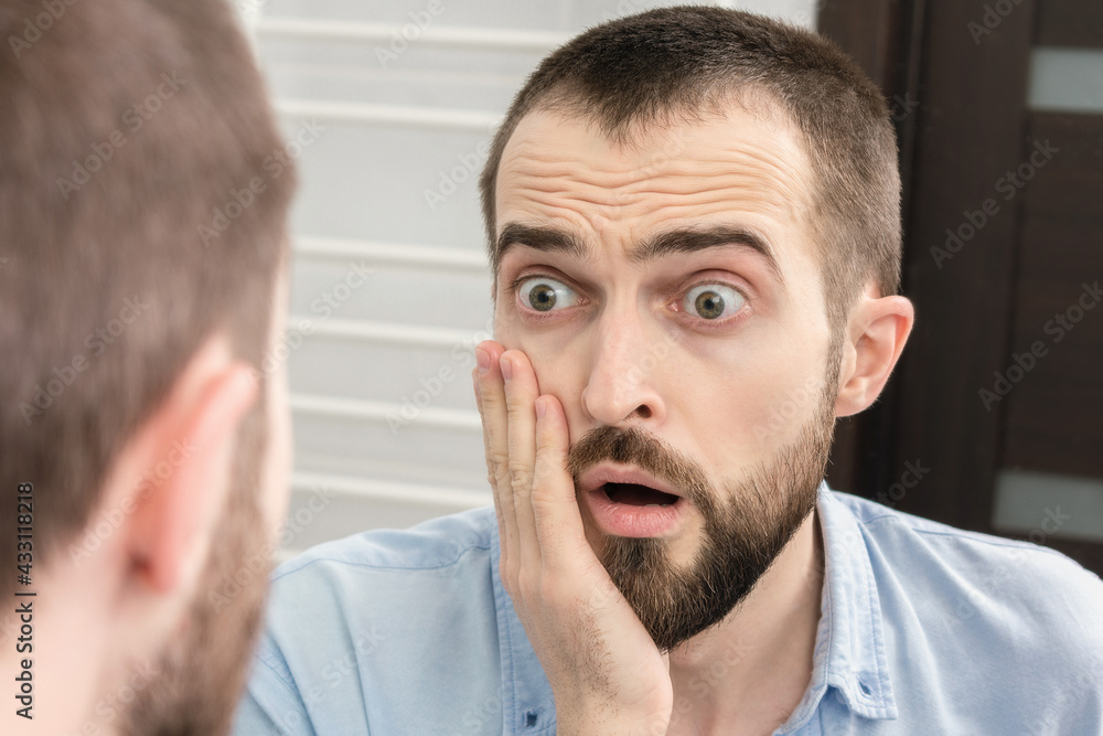 Fototapeta premium Shocked man seeing something surprising in bathroom mirror, portrait, closeup