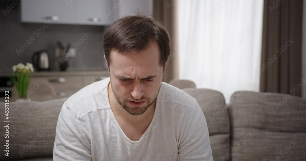 Man negatively angry angry worried about noise differently and negatively shows a gesture quietly pressing his finger to his lips sitting at home on the couch