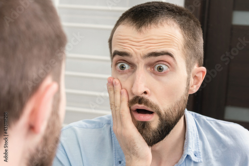 Shocked man seeing something surprising in bathroom mirror, portrait, closeup