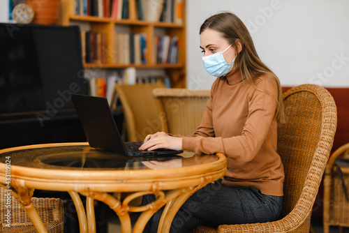 young girl in blue medical mask work in cafe on a laptop