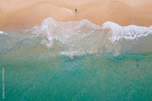 Aerial view of turquoise ocean wave reaching the coastline with lonely fisherman fishing on the beach. Beautiful tropical beach from top view. Andaman sea in Thailand. Summer holiday vacation concept