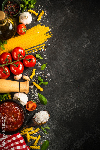 Italian food background. Pasta, olive oil, tomato sauce, spices, basil and fresh tomatoes. Top view with copy space.