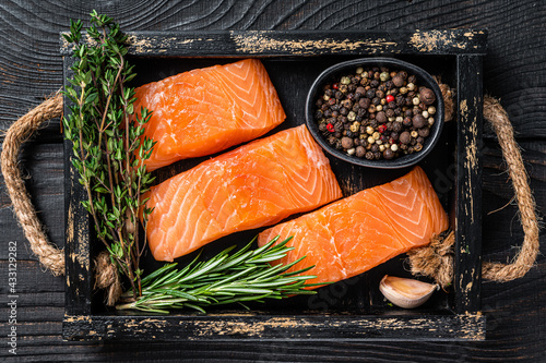 Raw salmon fillet fish steaks in a wooden tray with thyme and rosemary. Black wooden background. Top view