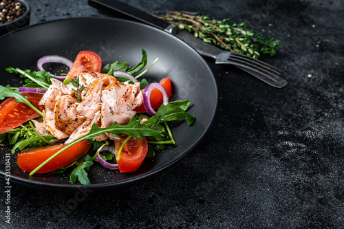 Salad with roasted salmon fillet steak, fresh salad arugula and tomato in a plate. Black background. Top view. Copy space