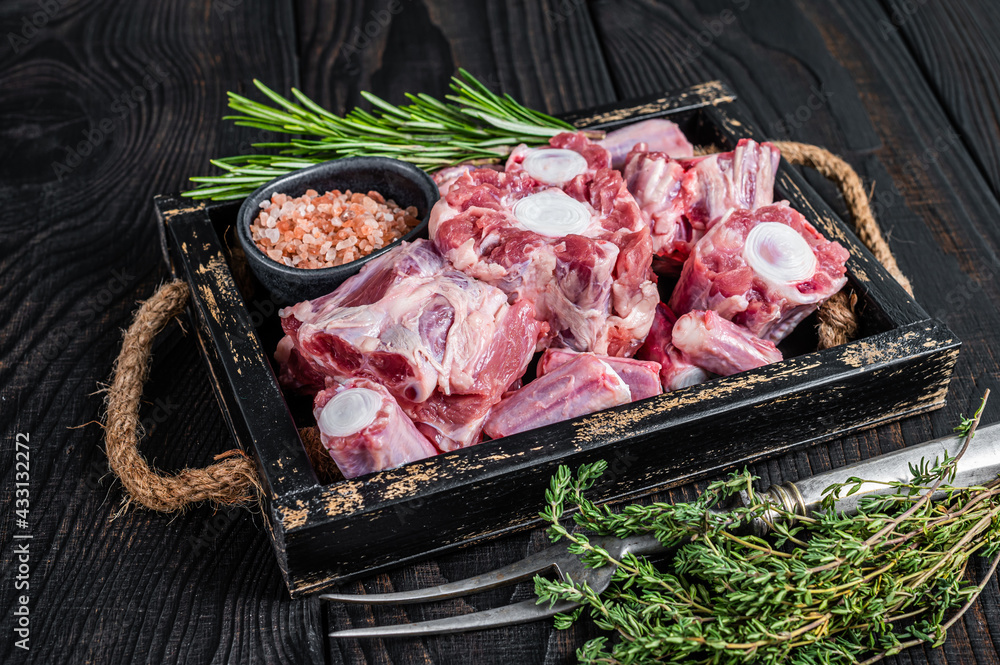 Raw veal beef Oxtail Meat in wooden tray with thyme. Black wooden background. Top view