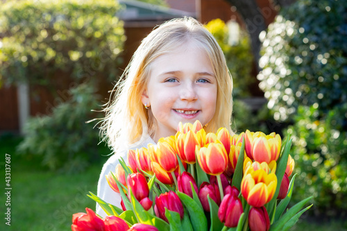 Cute adorable smiling toothless little girl with a huge bunch of tulips. Girl getting flowers. Picking flowers for gift bouquet in the garden. Mother's day, Birthday surprise. Happy childhood.