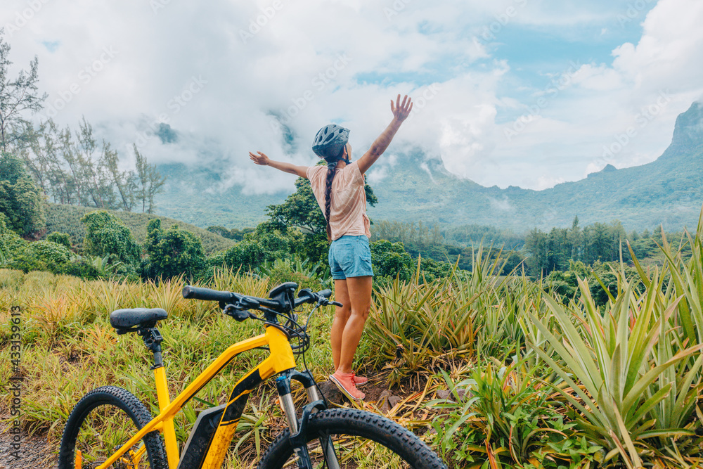 Mountain e biking happy girl with arms up of happiness traveling on Tahiti island with e-bike riding electric mtb bicycle on trail adventure. Travel summer lifestyle. Mountain e biking happy girl with arms up of happiness traveling on Tahiti island with e-bike riding electric mtb bicycle on trail adventure. Travel summer lifestyle.