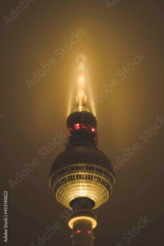 View of Famous Alexanderplatz TV Tower of Berlin, Germany in Colourful Yellow Golden light Color surrounded by Fog at Night, Close up View of Antenna