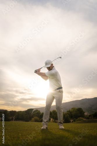 Golf player making a perfect swing on the golf course in the sunset.