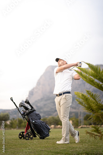 Golf player making a perfect swing on the golf course with his bag of clubs in the sunset.