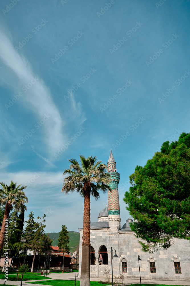 Green mosque (yesil camii) in Nicaea (iznik) during spring and sunny day in center of the city covered by many green plants, and palm trees and it turquoise color minaret